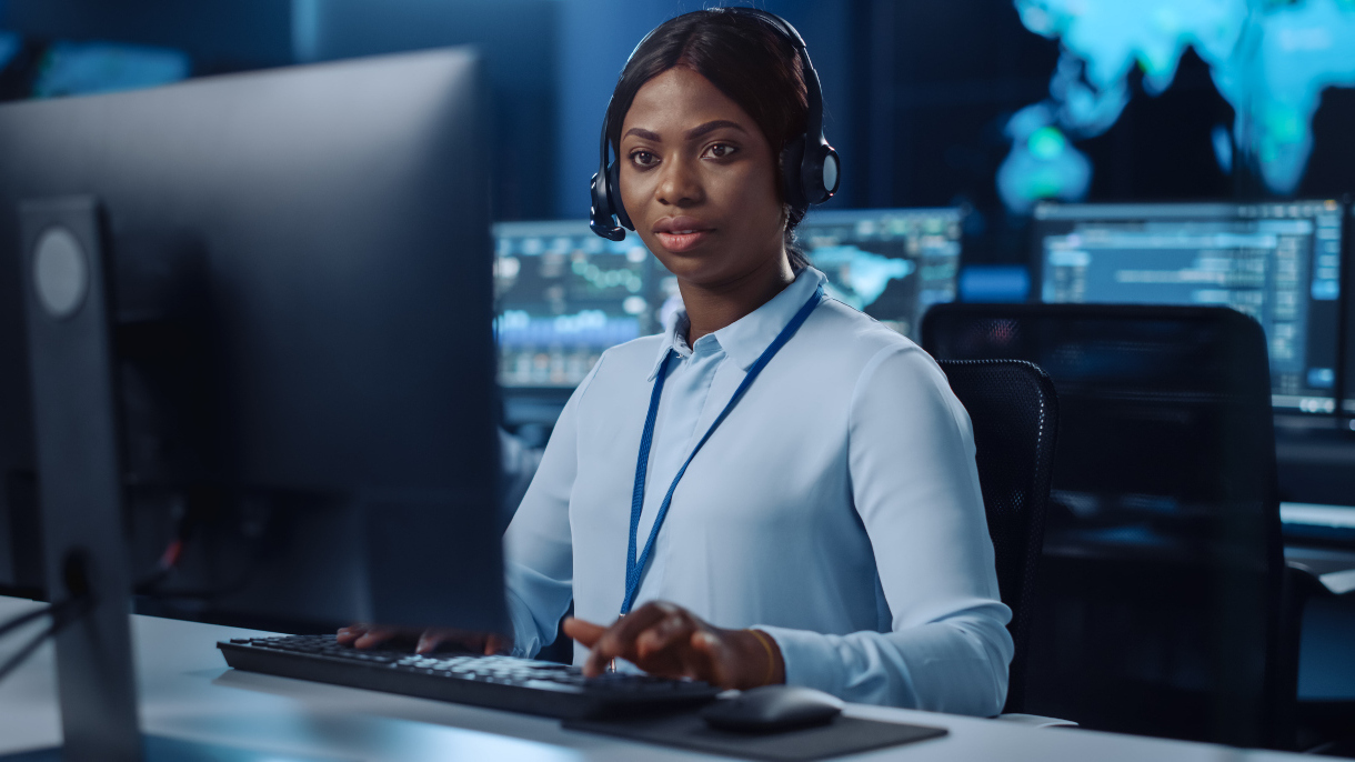 Joyful Beautiful Technical Customer Support Specialist is Talking on a Headset while Working on a Computer in a Call Center Control Room Filled with Colleagues, Display Screens and Data Servers.